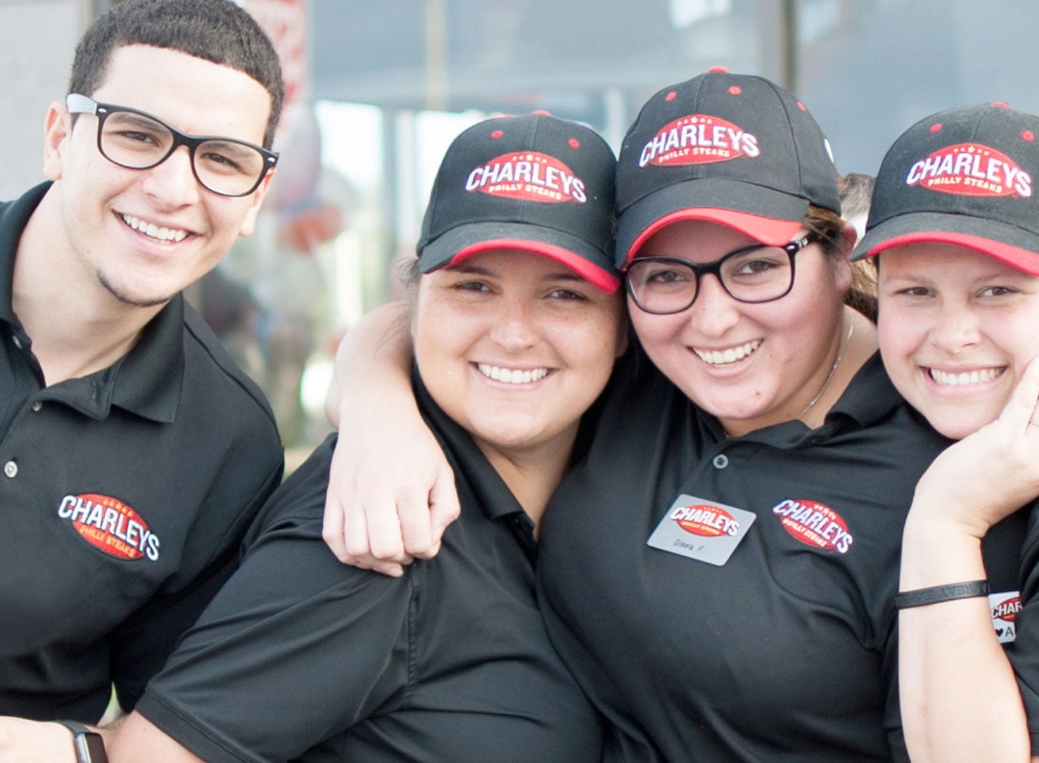 Four Charleys team members smiling and laughing while wearing uniforms. Learn more about Charleys careers.