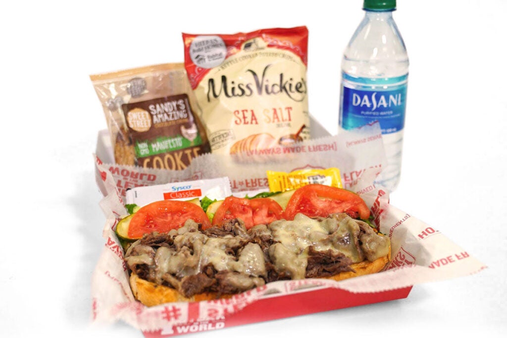 A catering boxed meal from Charleys Cheesesteaks. Charleys boxed meals include your choice of steak, chicken, or veggie cheesesteak, chips, a cookie, and a bottled water.