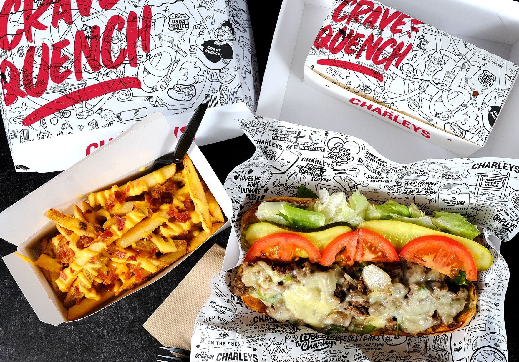 A Charleys Philly Steak Cheesesteak with Gourmet Fries and black and white packaging on a black table. Used to promote the Charleys Rewards app, where guests can get coupons and earn rewards on orders.