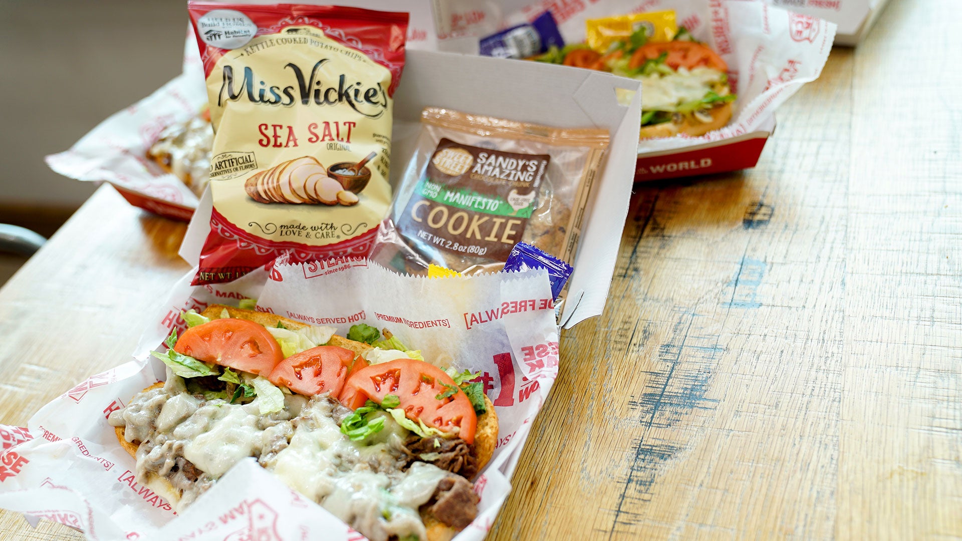 A catering lunch box for a catered event from Charleys Cheesesteaks, including a cheesesteak, chips, and a cookie.