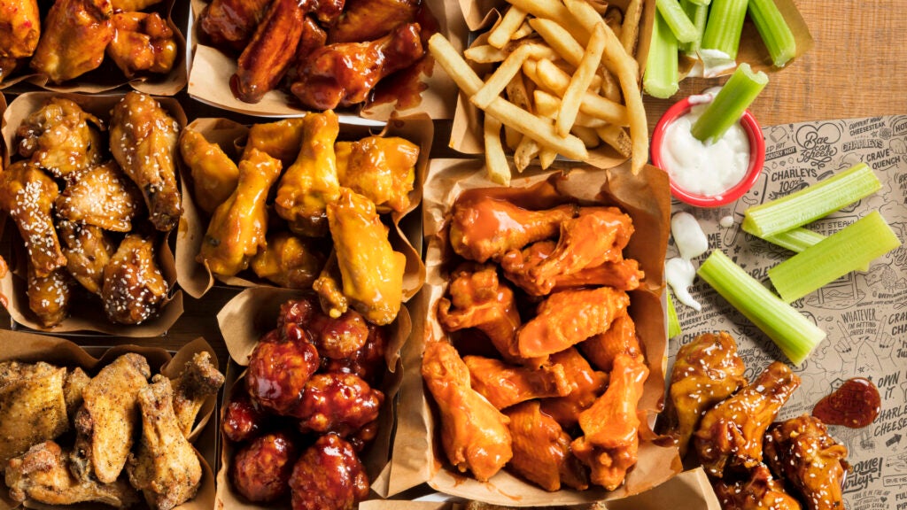 A spread of boneless and classic wings with dips on a wooden table. Catering, box lunch.