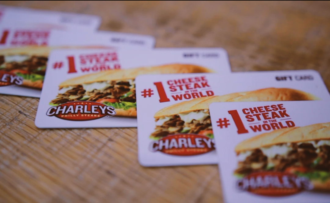 Four Charleys Cheesesteaks gift cards displayed on a wooden table.