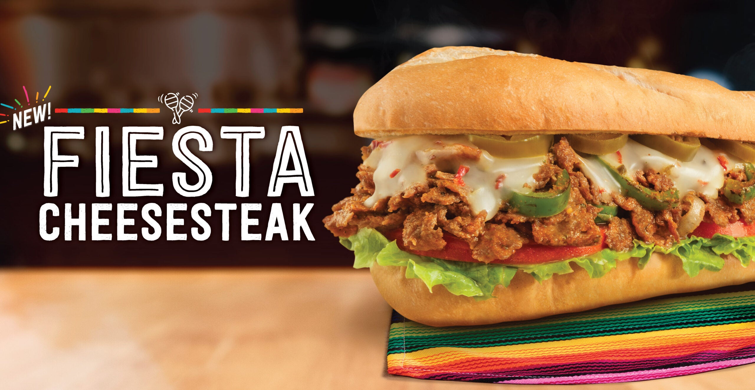 The Fiesta Cheesesteak from Charleys Cheesesteaks on a colorful placement, with white text reading "Fiesta Cheesesteak".