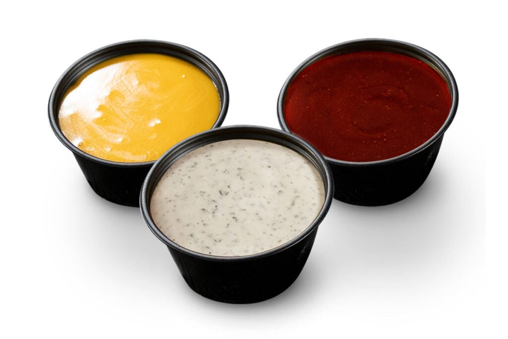 Three small cups of extra sauce from Charleys Cheesesteaks, including cheddar cheese, barbecue, and ranch dressing.