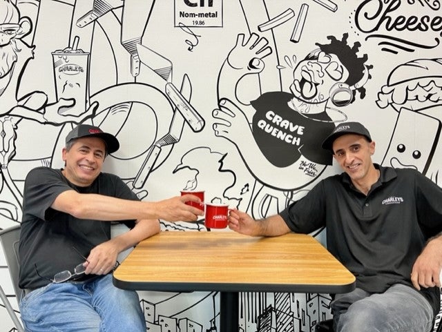 Charleys franchise owners at Bonney Lake, WA sitting at a table and clinking mugs in front of a mural.