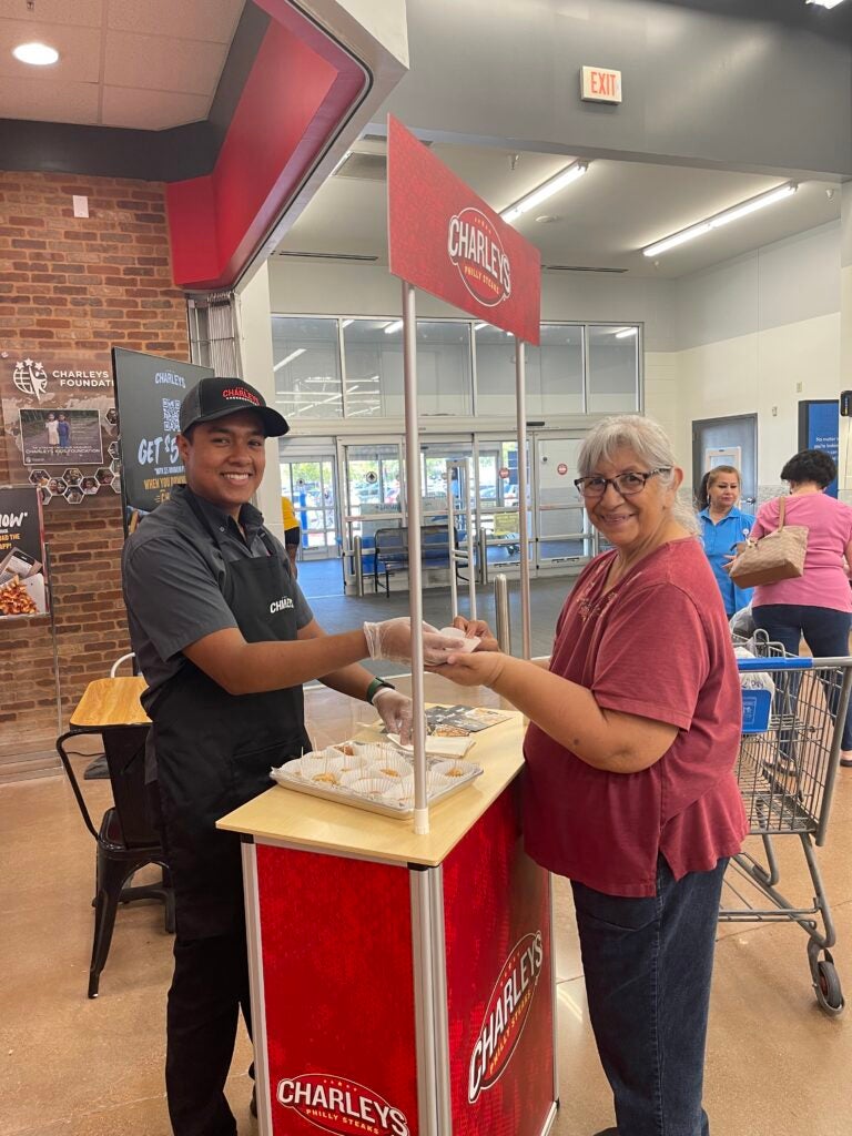 A team member handing out free samples of cheesesteaks to a guest near Walmart's front entrance.