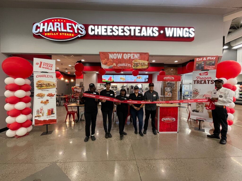 The team at Charleys Cheesesteaks and Wings standing in front of the menu and front counter, surrounded by balloons and ribbons to celebrate their grand opening.