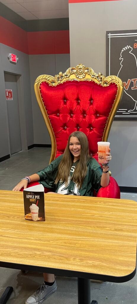 A young girl holding a Strawberry Lemonade, sitting in a red stuffed chair at Charleys Cheesesteaks and Wings.