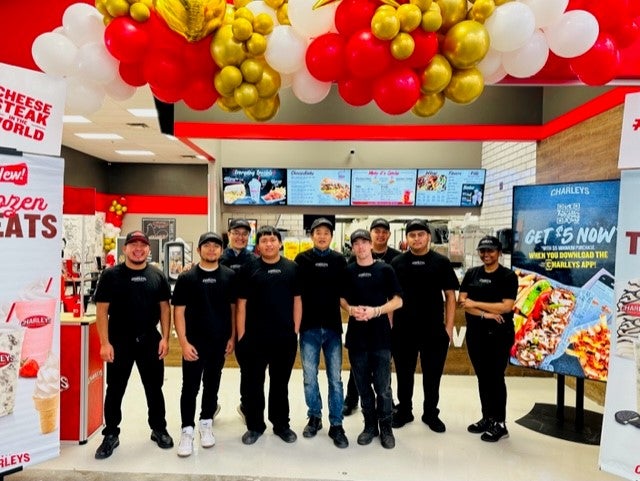 The team at the grand opening of Charleys Cheesesteaks and Wings at Belle Isle Blvd. Walmart. This includes people standing in front of the entrance to Charleys surrounded by signs and balloons for the grand opening.